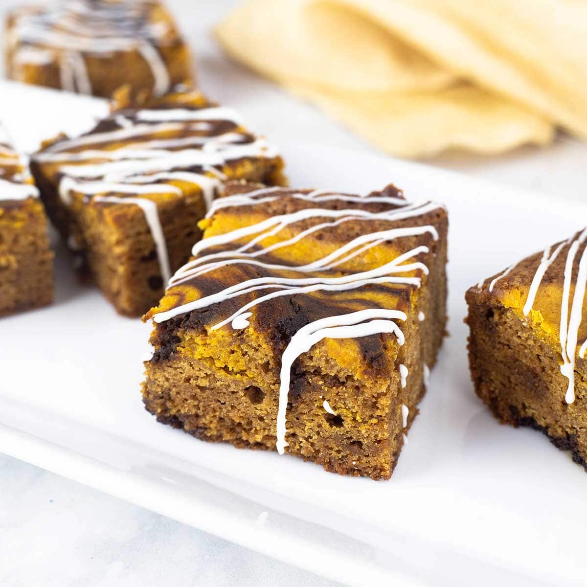 Gingerbread brownies with a white chocolate drizzle on a white plate with a gold napkin in the background.