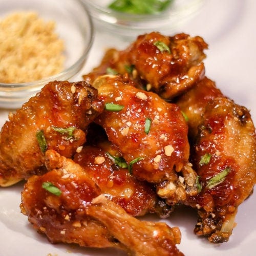 Asian Sticky Wings on a plate next to crushed peanuts and chopped green onions