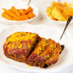 Cheesy Meatloaf sliced on a white platter with carrots and potatoes
