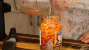 pouring pickling liquid into a jar of sliced vegetables for pickled vegetables