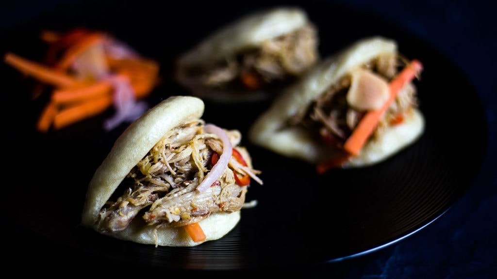 Asian Steamed buns sitting on a plate filled with Asian Pulled Pork and Pickled Vegetables
