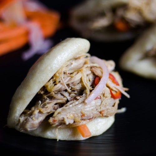 Asian Steamed Buns on a plate stuffed with Asian Pulled Pork and pickled vegetables