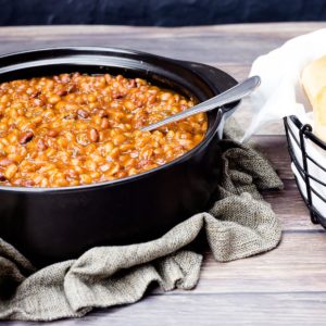 Pressure cooker baked beans in a black pot with a serving spoon