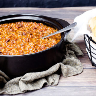 Pressure cooker baked beans in a black pot with a serving spoon
