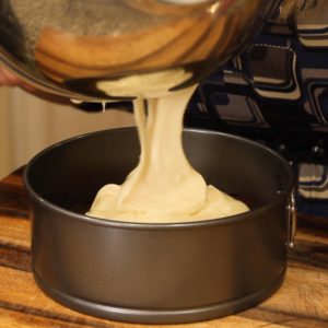 pouring cheesecake batter onto brownie crust for Turtle Cheesecake Recipe