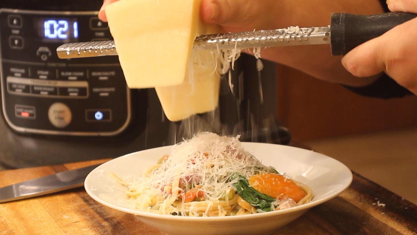 grating Parmesan over a bowl of one pot pasta primavera
