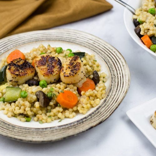 seared scallops on a bed of pearled couscous and vegetables.