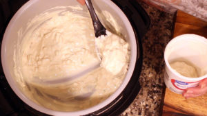 scooping the homemade french onion dip out of the inner pot into the empty sour cream container for storage