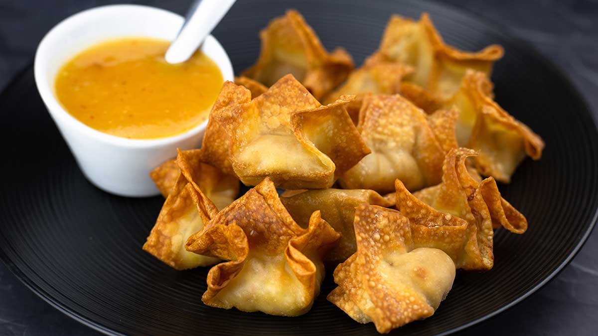 Air Fryer Crab Rangoon sitting next to a pineapple sweet and sour souce