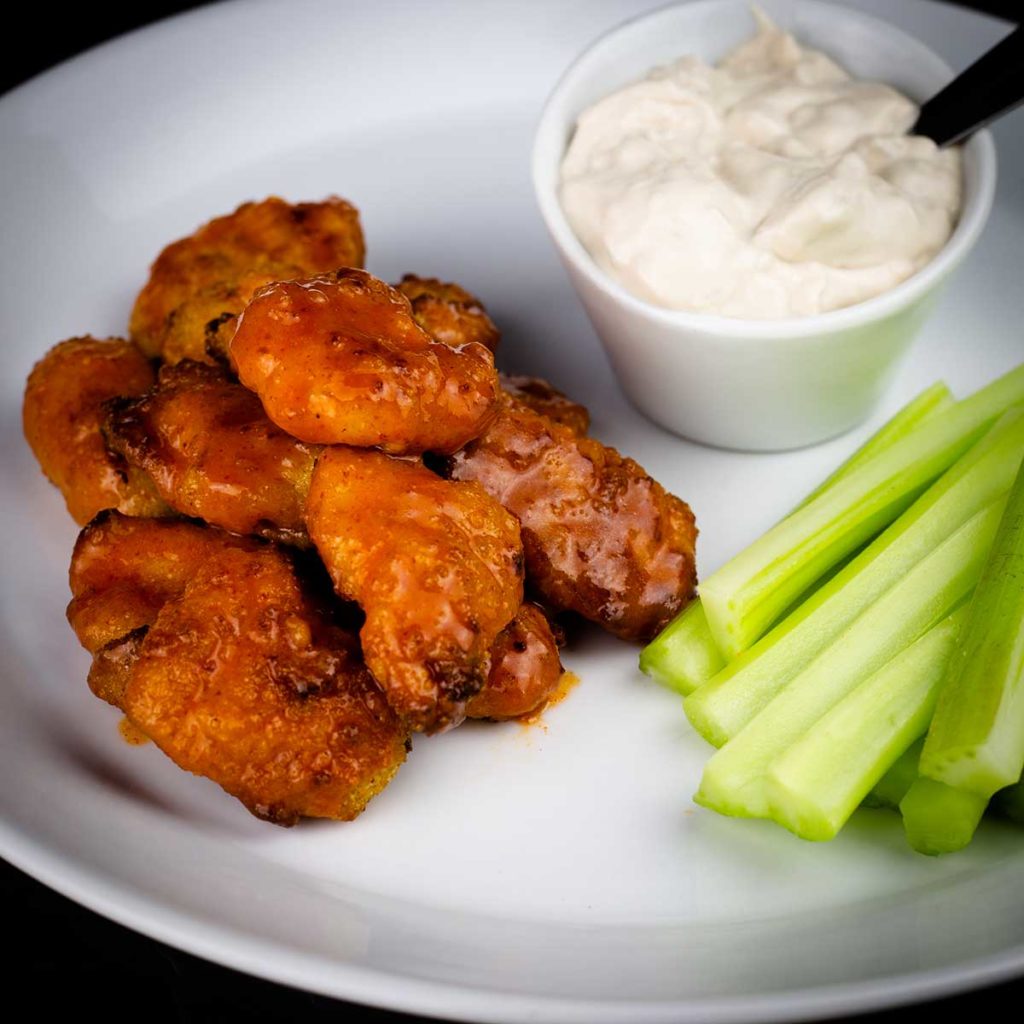 Boneless buffalo wings on a white plate with celery and blue cheese dressing