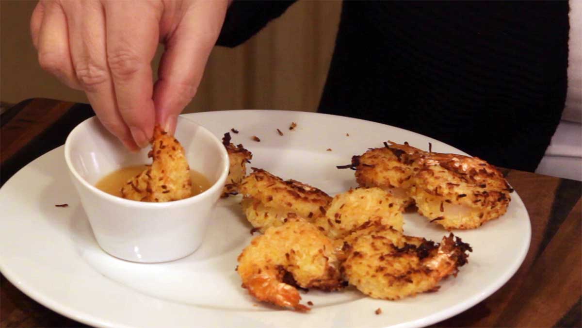dipping the finished coconut shrimp in pineapple sweet and sour sauce
