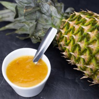 pineapple sweet and sour sauce in a white bowl with a spoon and a pineapple in the background