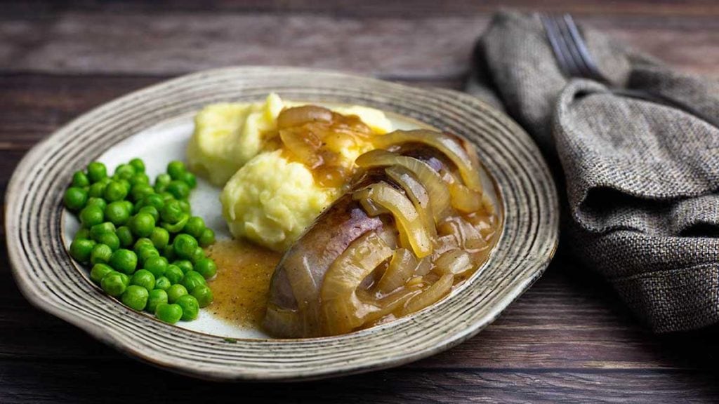 bangers and mash on a plate with onion gravy and peas
