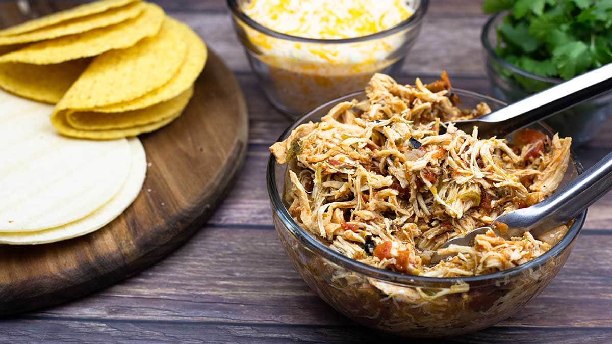 Mexican Shredded Chicken in a bowl next to tortillas, cheese, and cilantro