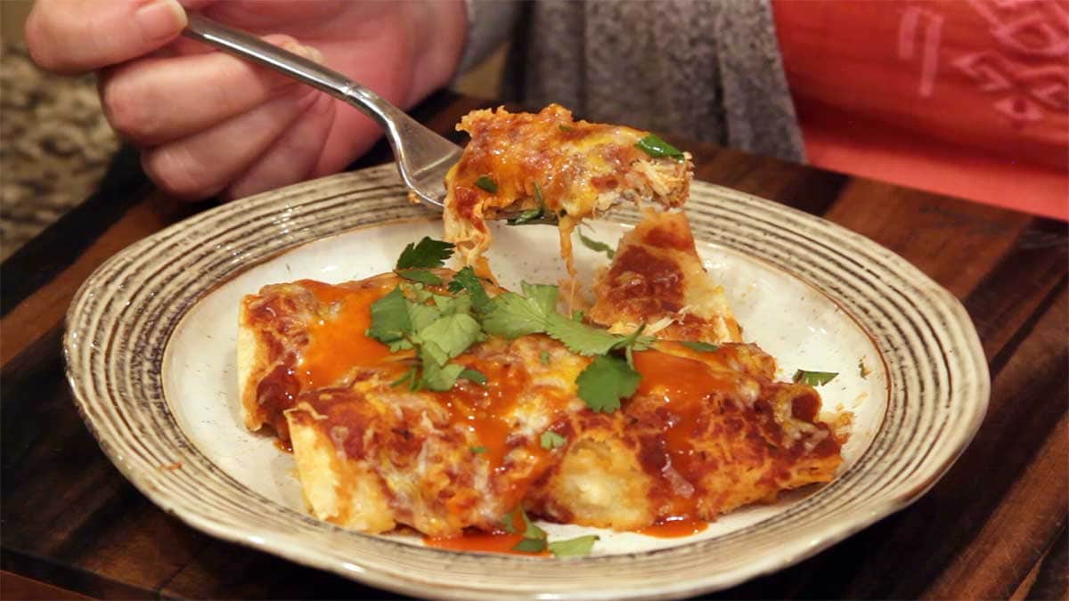 homemade chicken enchiladas on a plate with a bite on a fork