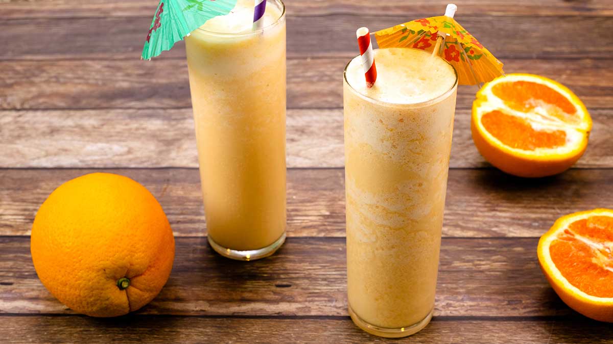 Pomerančové mléčné koktejly s plátky pomeranče vedle sebe a plným pomerančem