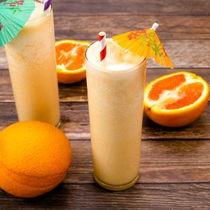 Sinaasappelmilkshakes met in plakjes gesneden sinaasappels ernaast en een volle sinaasappel