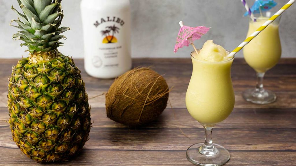 Pina Colada in a glass next to a pineapple and coconut