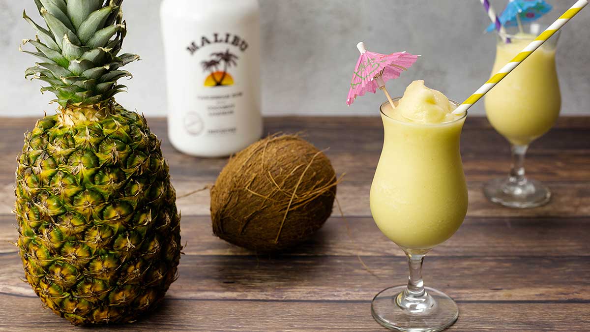 Pina Colada in a glass next to a pineapple and coconut