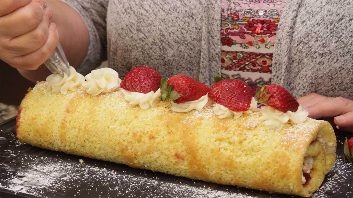 Decorating the Strawberry Roll Cake with buttercream dollops and fresh strawberries