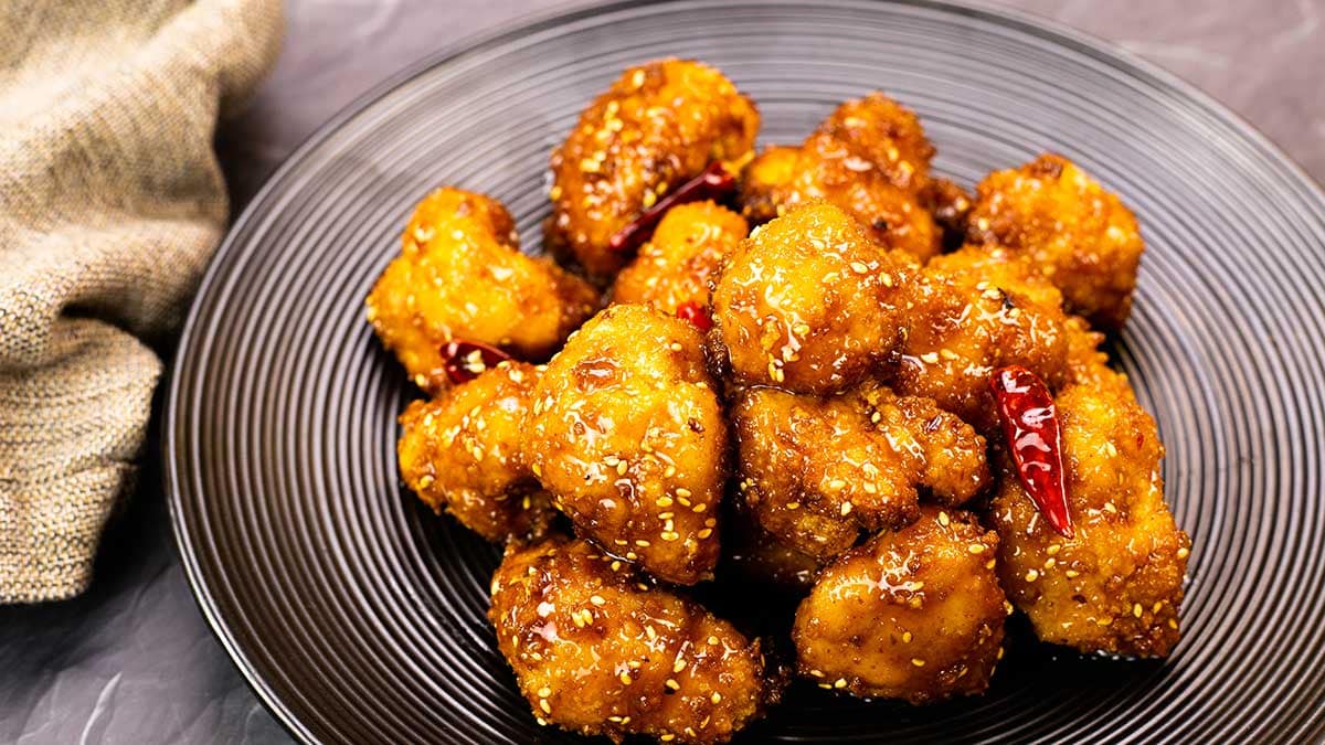 Air Fried Cauliflower tossed in General Tso's Sauce on a black plate