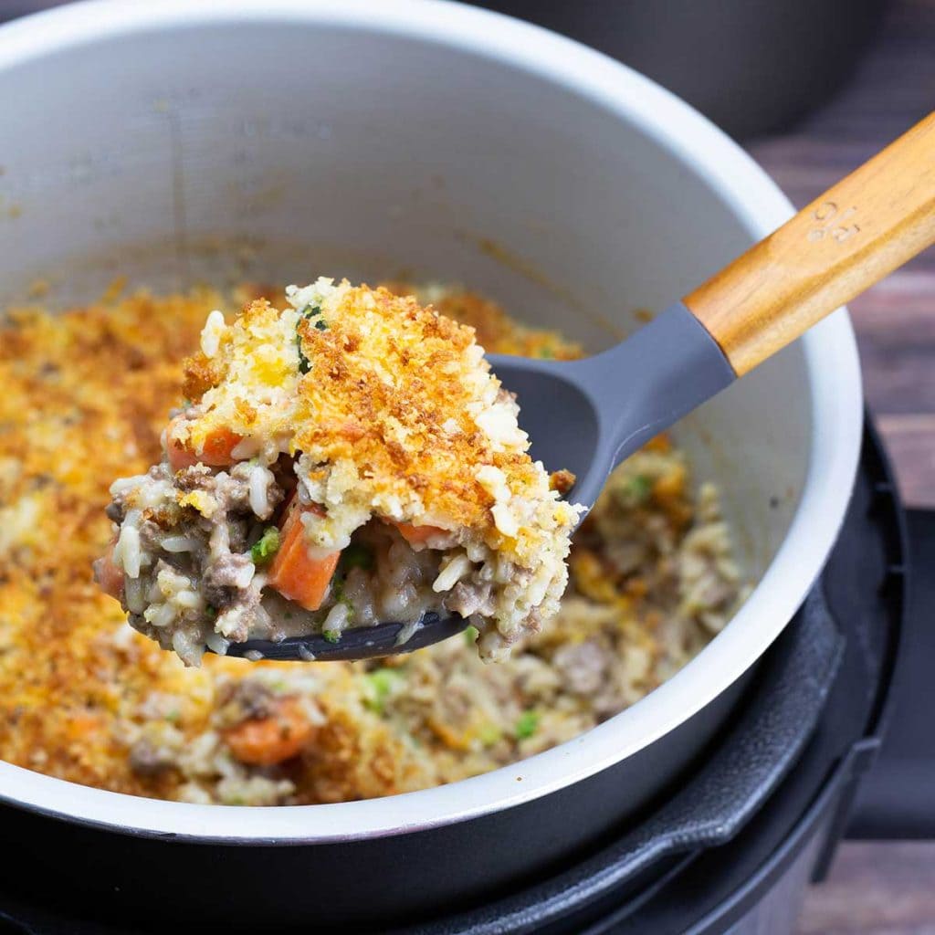 Cheesy Ground Beef and Rice Casserole in the Inner pot with a large spoon lifting out a serving