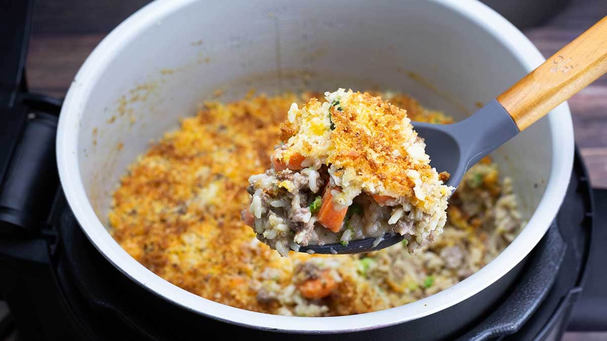 Cheesy Ground Beef and Rice Casserole in the Inner pot with a large spoon lifting out a serving