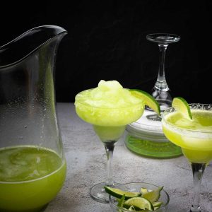 cucumber jalapeno margaritas both frozen and on the rocks in glasses next to a pitcher of margarita mix