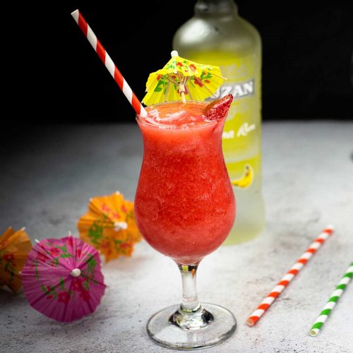 Frozen Strawberry Daiquiri in a hurricane glass with colored straws and drink umbrellas