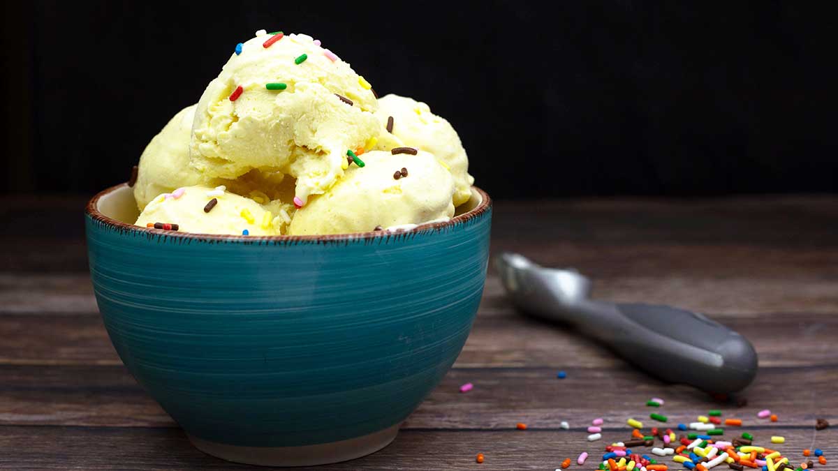 Scoops of vanilla ice cream in a blue bowl with colorful sprinkles on top