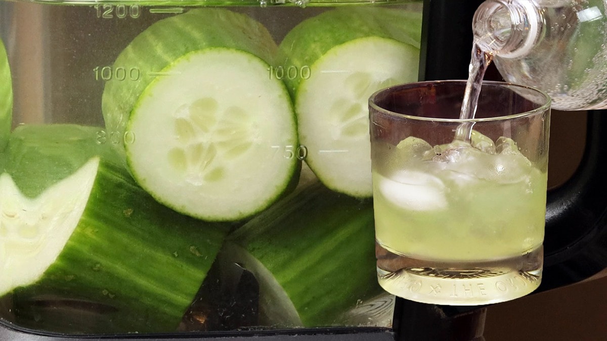 cucumber infused vodka in a glass with cucumbers in the blender behind it