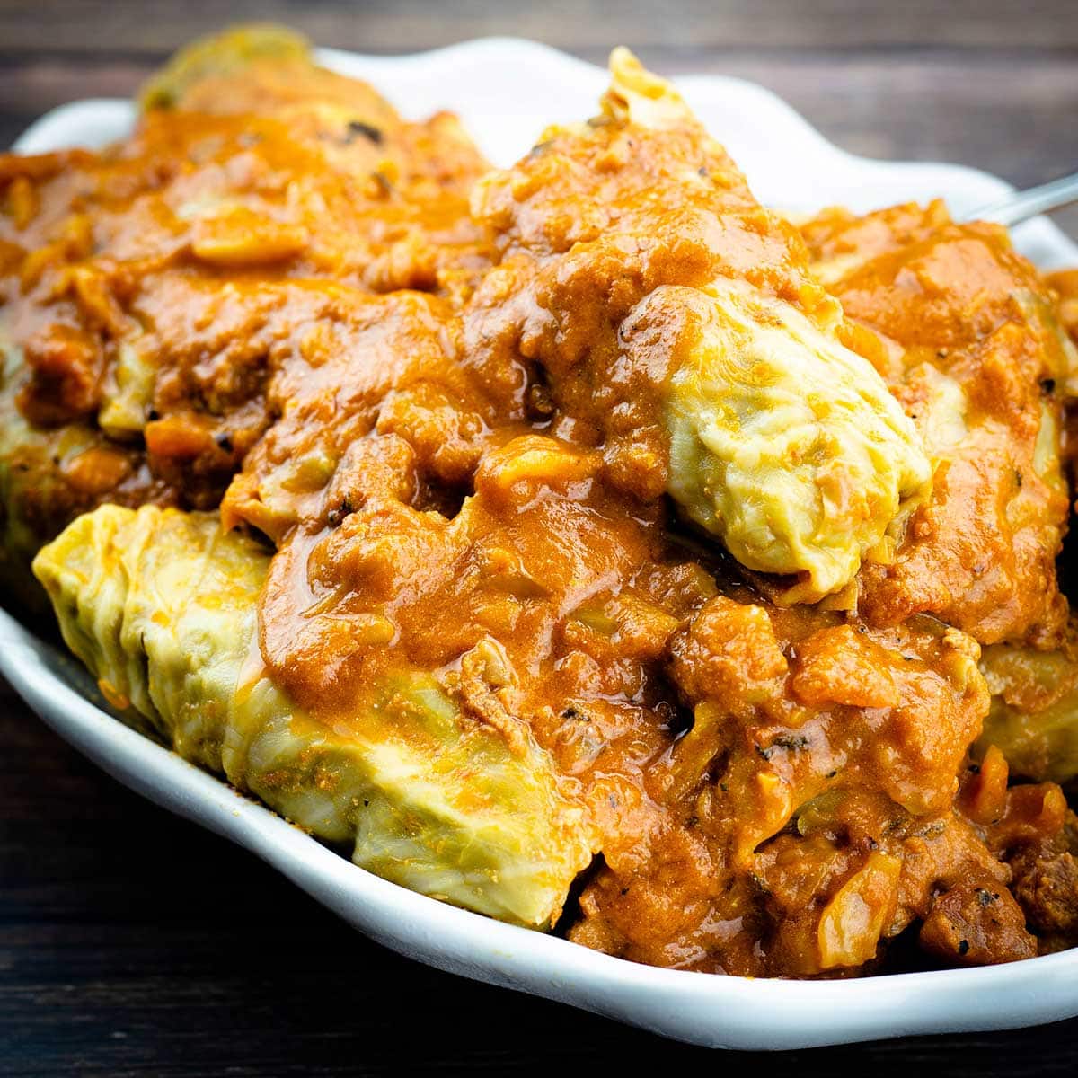 cabbage rolls with sauce over top in a white serving platter