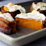 bacon wrapped candied sweet potatoes on a tray with one cut in. half