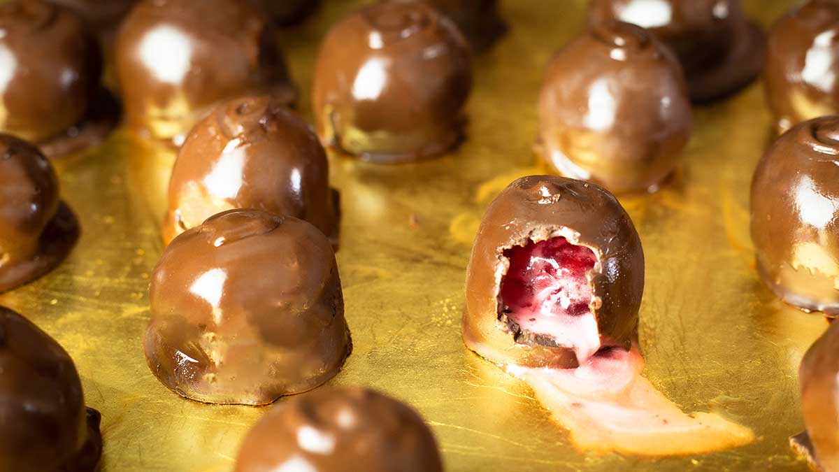 tray of chocolate covered cherries with one opened and the liquid center dripping out