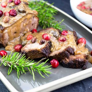 sliced brisket on a platter with gravy and cranberries