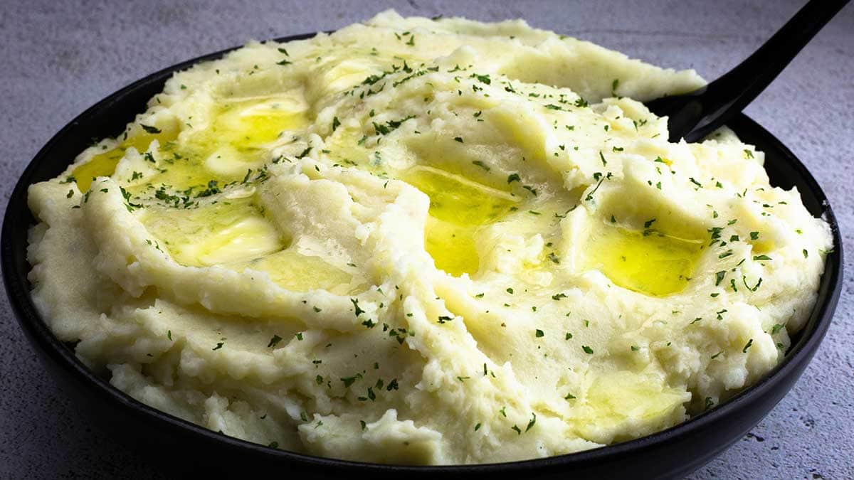 creamy mashed potatoes in a black bowl with butter melting on top