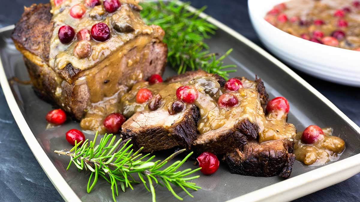 sliced brisket on a platter with gravy and cranberries