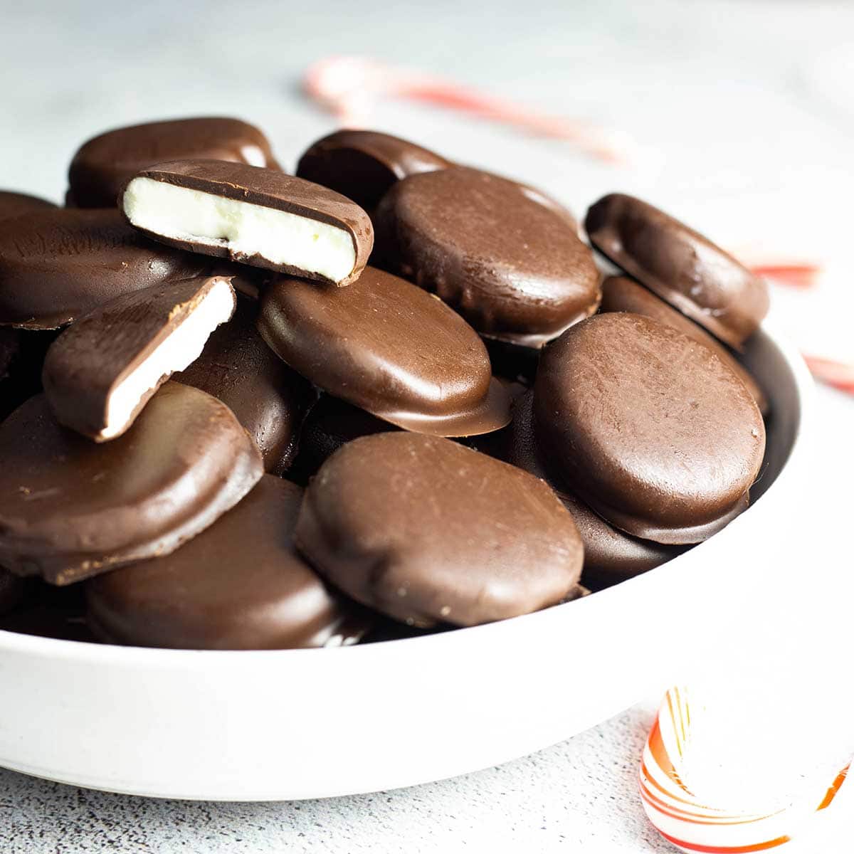 Peppermint patties in a white bowl with candy canes next to it