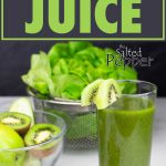 Green juice in a glass with fruit and vegetables behind it