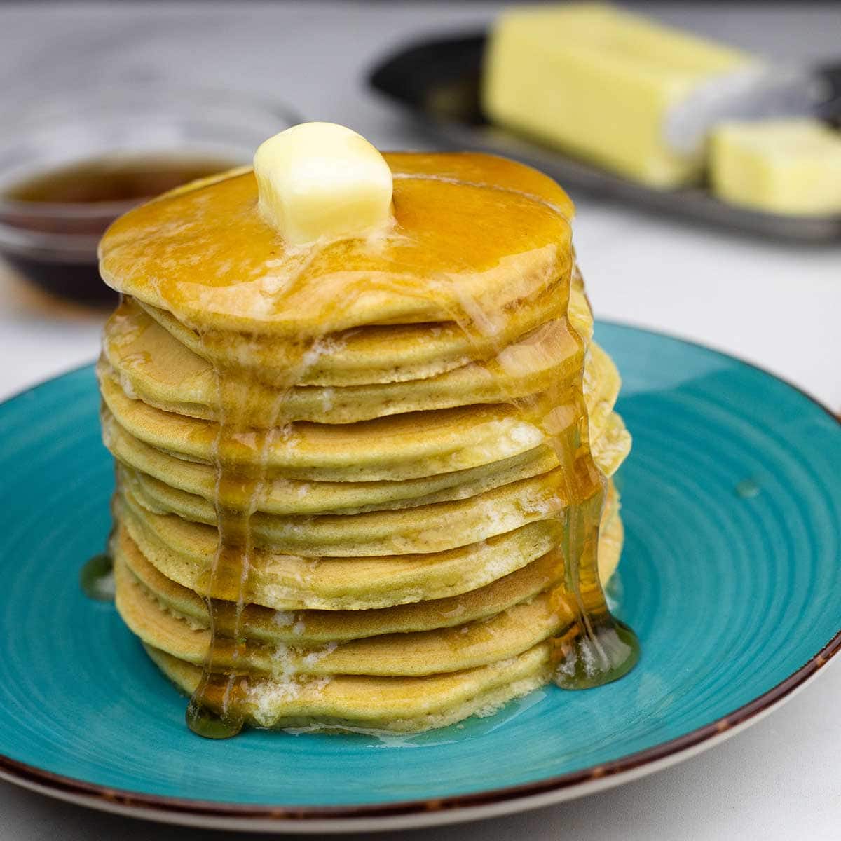 Keto pancakes stacked on a blue plate with butter and syrup dripping down the sides