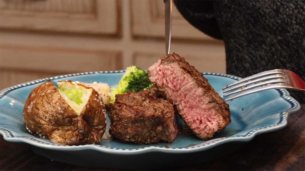 medium rare steak cut in half on plate with broccoli and potato and scallops