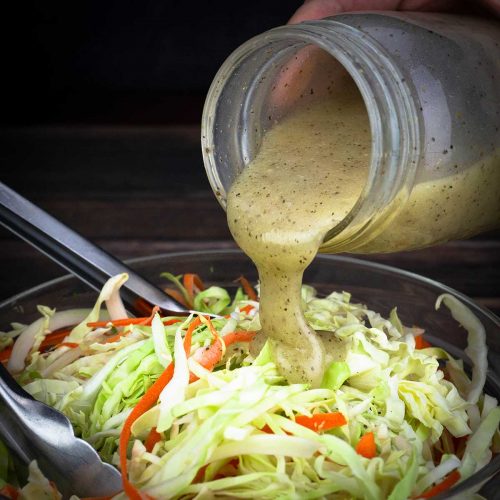 creamy coleslaw dressing being poured over shredded cabbage and carrots