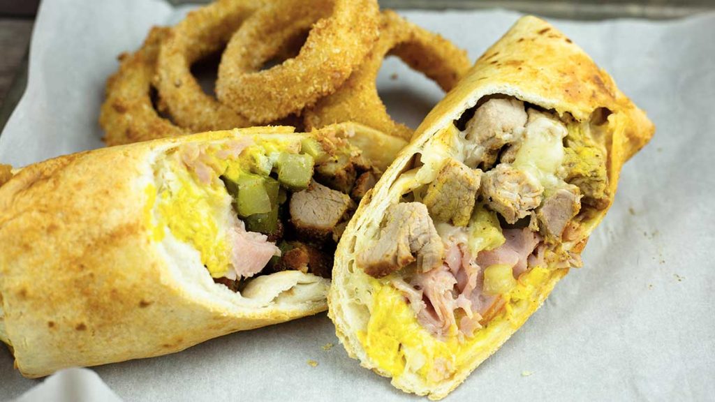 Air Fryer Cuban Wrap cut in half on parchment with onion rings behind it