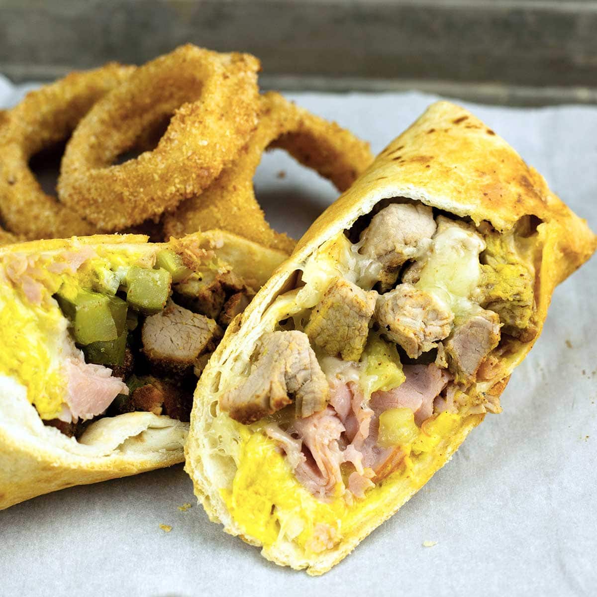 Air Fryer Cuban Wrap cut in half on parchment with onion rings behind it