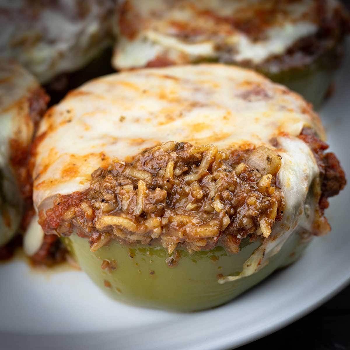 Stuffed peppers on a white plate with cheese melted on top