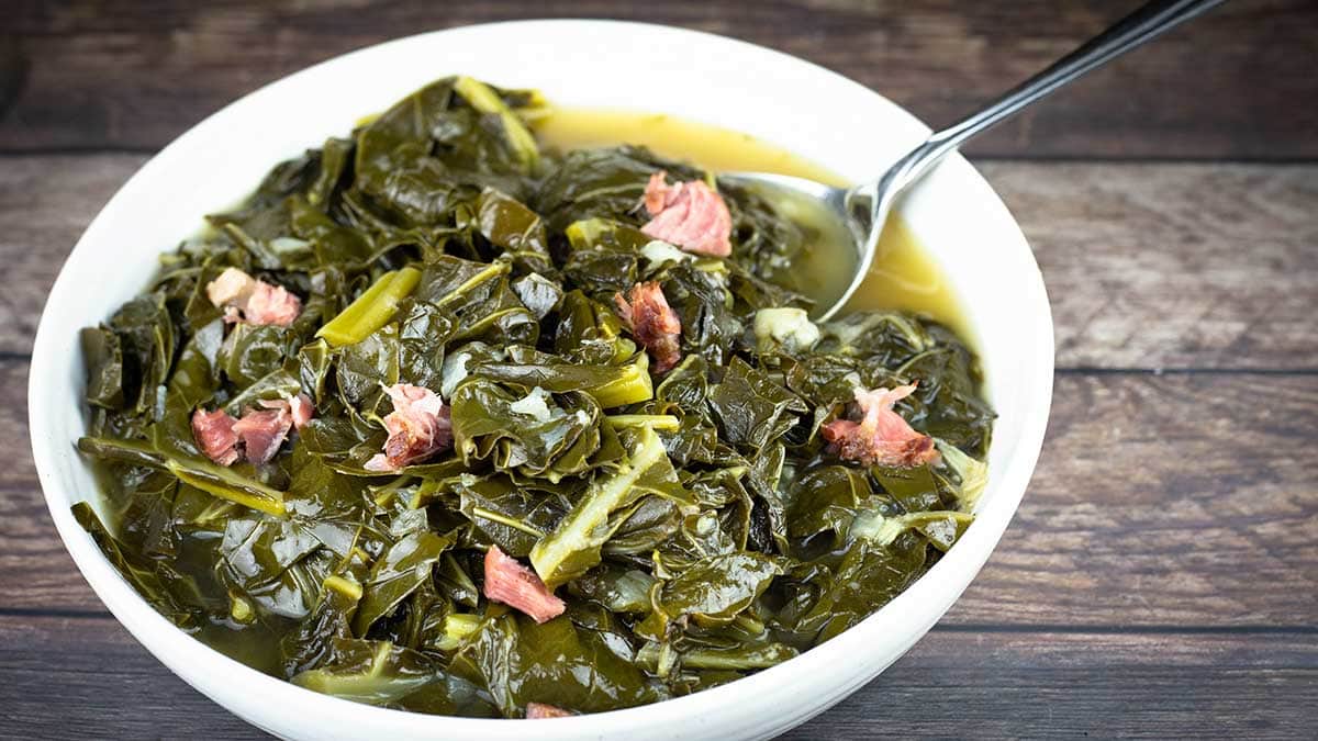 collard greens with broth in a white bowl with a serving spoon