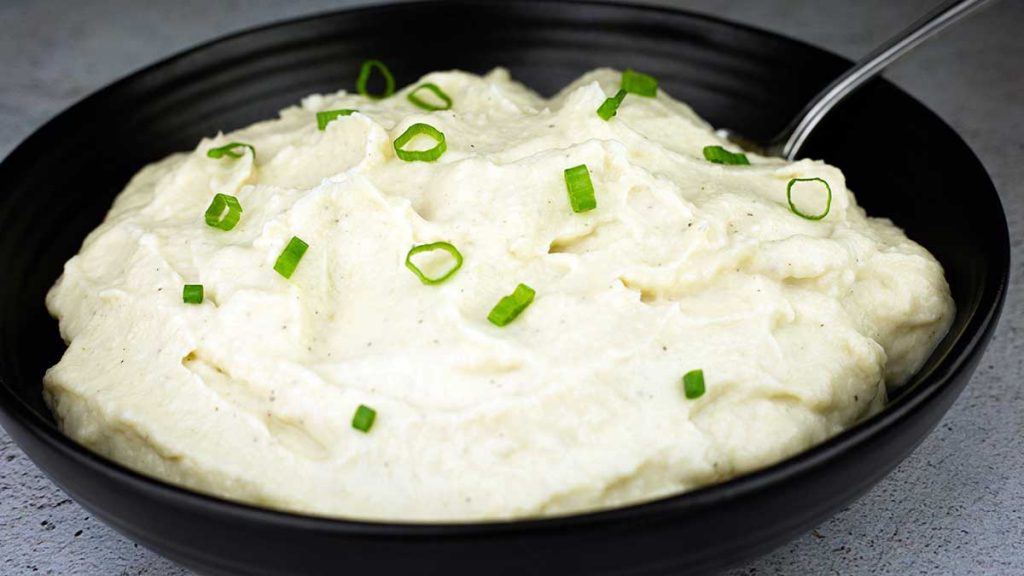 mashed cauliflower in a black bowl with green onions on top