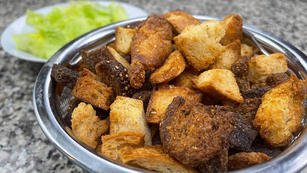 air fryer croutons in a wire strainer with a salad behind them
