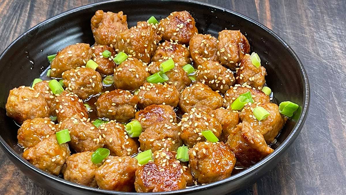 Asian turkey meatballs in a black bowl with sesame seeds and green onions as garnish
