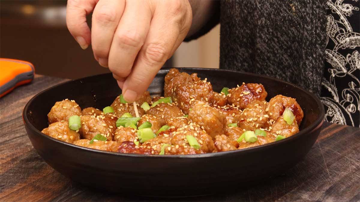asian turkey meatball in black bowl taking one out with toothpick